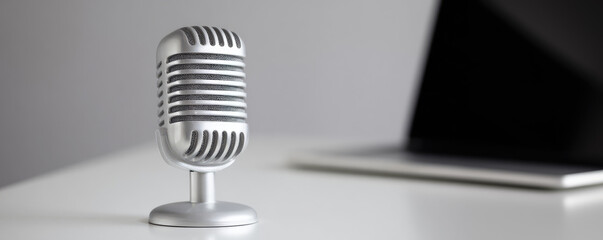 A vintage-style microphone is on a white desk near a partly visible laptop. Concept: podcasting, broadcasting, audio recording
