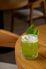 A vibrant green drink sits atop a polished wooden table, showcasing fresh mint leaves and a slice of lime. The warmth of the wood contrasts beautifully with the cold beverage
