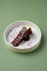 Delightful cheesecake adorned with smooth chocolate sauce and vibrant raspberry crumbles sits on a minimalist, muted green plate. This treat captures both elegance and indulgence