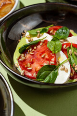 Slices of creamy mozzarella and ripe tomatoes are artfully arranged, topped with fresh spinach and crunchy toasted seeds, showcasing vibrant colors and textures