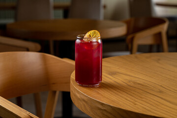 A vibrant drink rests on a polished wooden table, adorned with a slice of dried fruit, embodying warmth and comfort in an inviting cafe atmosphere during midday