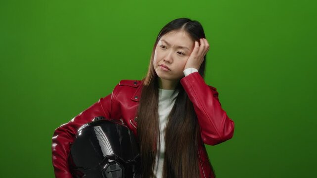 Woman thinking wearing red jacket holding helmet against green background looks contemplative and stylish