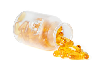 Frosted glass jar tipped over with golden fish oil softgel capsules spilling out isolated on white background.