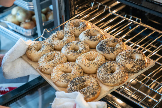 Raw bagel dough covered in everything seasoning and sesame seeds going into an oven 