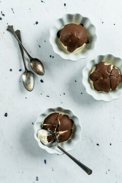 Single scoop vanilla ice cream in white bowls with chocolate shell on top 