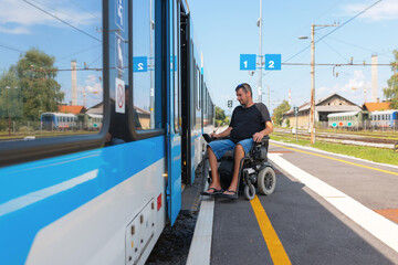 Man with disability navigates his wheelchair towards a tram at a train transportation station on a clear day. The setting features blue signage and a welcoming atmosphere.