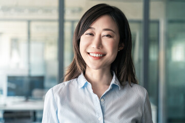 Headshot close-up portrait of mature Asian good looking middle-aged leader, ceo female businesswoman on office background. Beautiful executive manager, business sales leader woman smiling at camera.
