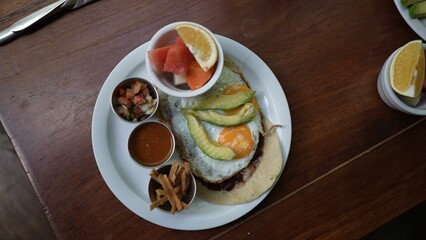 A middle-aged woman sits at a cafe table, savoring a colorful plate of breakfast food while engaging in work activities during her vacation.