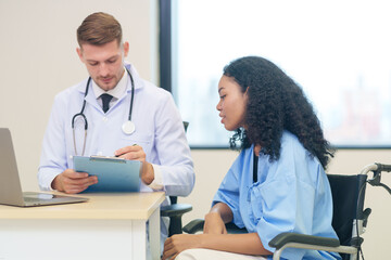 doctor in white gown with stethoscope,asking a woman patient on wheelchair a present illness and writing paper on clipboard to diagnosis and treatment
