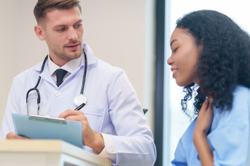 doctor in white gown with stethoscope,asking a woman patient on wheelchair a present illness and writing paper on clipboard to diagnosis and treatment