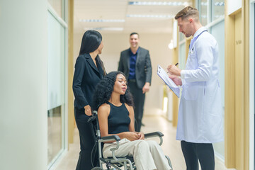 sick african business woman sitting on wheelchair at corridor with asian woman assistant and colleagues walking to encourage her,getting service at examine room in hospital