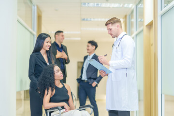 sick african business woman sitting on wheelchair at corridor with asian woman assistant,getting service at examine room in hospital