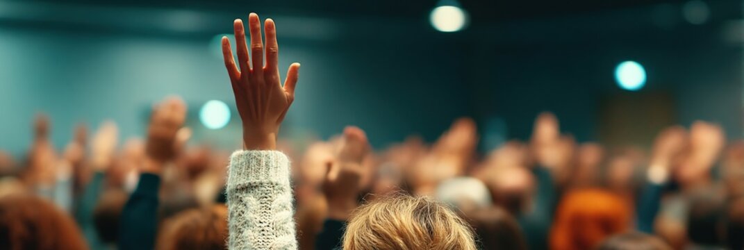 People raising their hands in a crowded room, possibly participating in a meeting, seminar, or voting session.