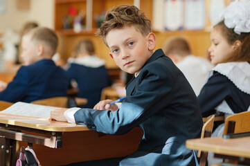 A first-grader boy is sitting at a desk in a classroom, the beginning of the school year. Back to...