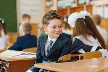 A first-grader boy is sitting at a desk in a classroom, the beginning of the school year. Back to...