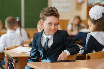 A first-grader boy is sitting at a desk in a classroom, the beginning of the school year. Back to...
