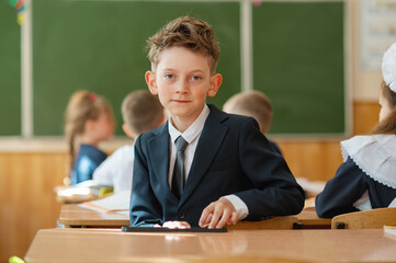 A first-grader boy is sitting at a desk in a classroom, the beginning of the school year. Back to school