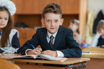A first-grader boy is sitting at a desk in a classroom, the beginning of the school year. Back to...