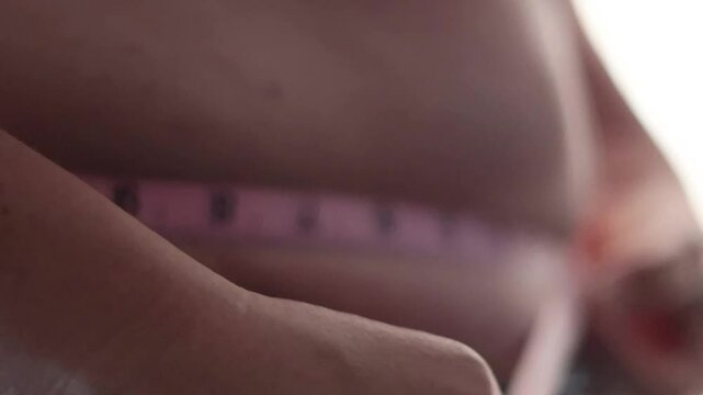 Un primer plano de una mujer blanca mayor de 50 a&ntilde;os midi&eacute;ndose el exceso de grasa abdominal con una cinta metrica, presenta problemas de sobrepeso 