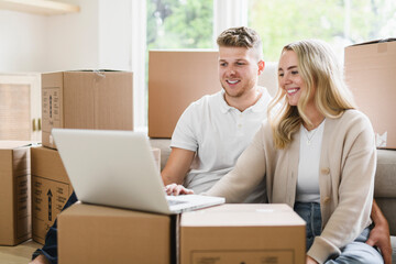 Young couple moving in new home. Couple is having fun with cardboard boxes in new house at moving...