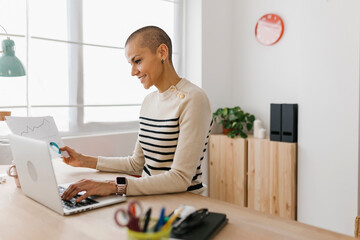 Businesswoman working with laptop while holding paperwork document on desk in the office