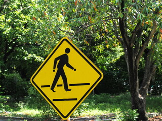 Pedestrian Crossing or Crosswalk installed in the park. Yellow iron sign with black edge with black pedestrian symbol on yellow background. Pedestrian Crossing or Crosswalk installed in the park. Yell