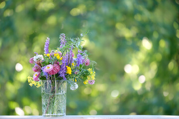 colorful meadow flowers in glass tumbler close up on table in garden, natural abstract background. Summer season. Beautiful floral composition.