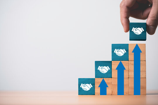 Hand stacking Hand shaking icon which print screen on wooden cube block on the top of up arrow for increasing business deal and agreement concept.