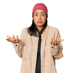 Young Filipino woman in studio doubting and shrugging shoulders in questioning gesture.