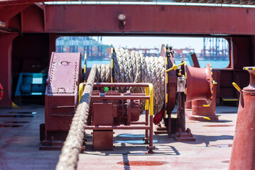 Large mooring winch on a ship's deck, featuring thick, braided ropes wound around a cylindrical metal drum. 