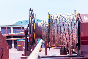 Close-up of mooring rope on a unfocused large mooring winch on the bow of a cargo ship.