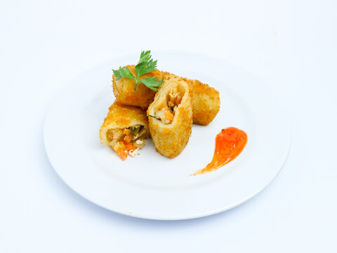 Crispy vegetable risol cut open on a white plate, served with chili sauce. isolated on white background