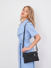 Blonde woman in profile wearing a light blue dress with a black crossbody bag, looking over...
