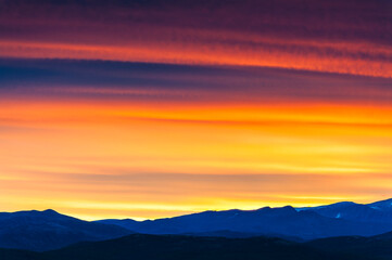 Vibrant sunset paints the sky over distant mountains in Norway