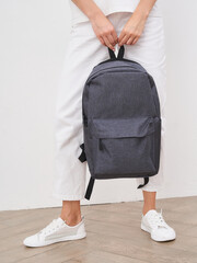 Gray backpack held by a person wearing white pants and white sneakers. The backpack has a front...