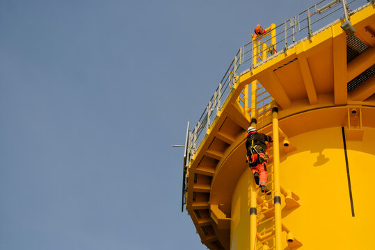 GWO-Certified Offshore Technician Rigger Climbing Wind Turbine Foundation Ladder Wearing Safety PPE.