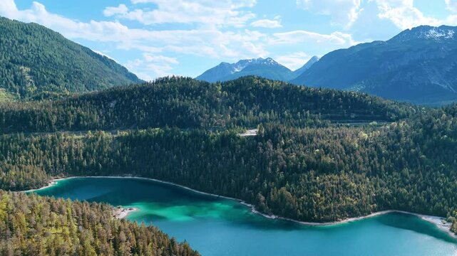 Beautiful turquoise lake surrounded by the rocks covered with pine-tree forests. Drone flight over the stunning wild nature of Europe.