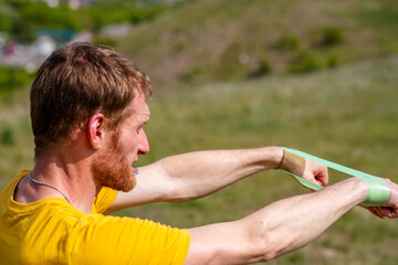 A professional sportsman in a yellow shirt is holding a Elastic band expander. He appears focused...