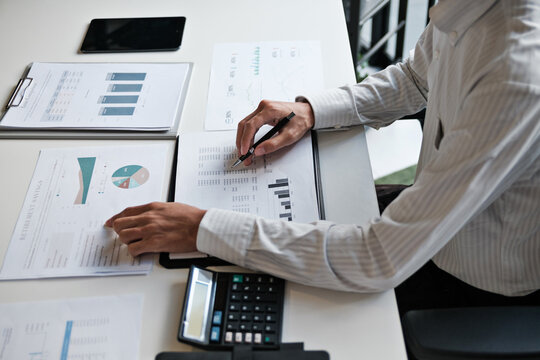 Administrative staff reviewing company budget report with calculator, document stack and focus at office desk