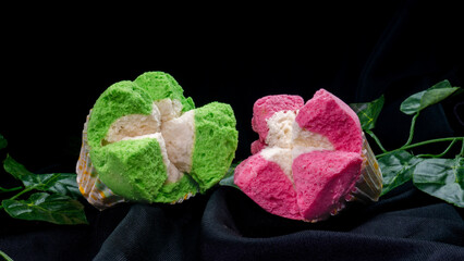 Two pink and green steamed sponge cakes in paper cups on black cloth and leaf decoration with dark...