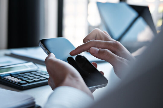Business professional reading business data on smartphone while sitting at desk in connected digital data at office
