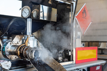 Open discharge outlet of a tanker truck carrying hazardous materials during the cleaning process at a wash station, releasing vapor and product residues.