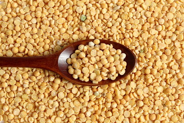 A wooden spoon with dry yellow peas lies on the surface.