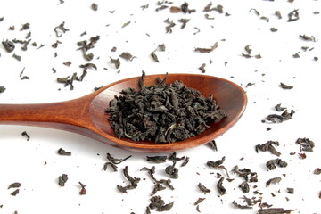 Dry tea leaves lie in a wooden spoon on a white background.	