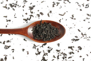 Dry tea leaves lie in a wooden spoon on a white background.