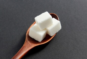 On a black background lies a wooden spoon with pieces of refined sugar.