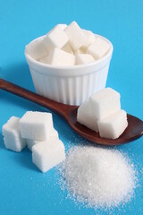 On a blue background there is a bowl with square sugar and a wooden spoon.	
