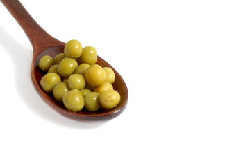 On a white background lies a wooden spoon with canned green peas.	