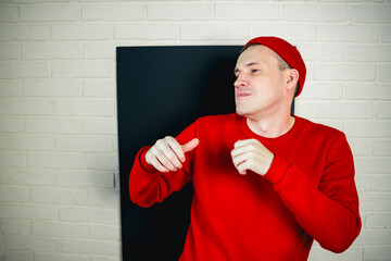 A man in a red hoodie and hat dances against a white brick wall