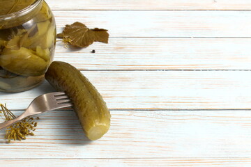  There is a glass jar with pickled cucumbers and a fork on the table.